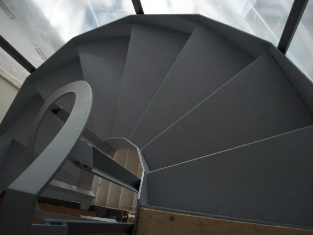 Grey steel spiral staircase with solid plate treads photographed looking down from the landing above