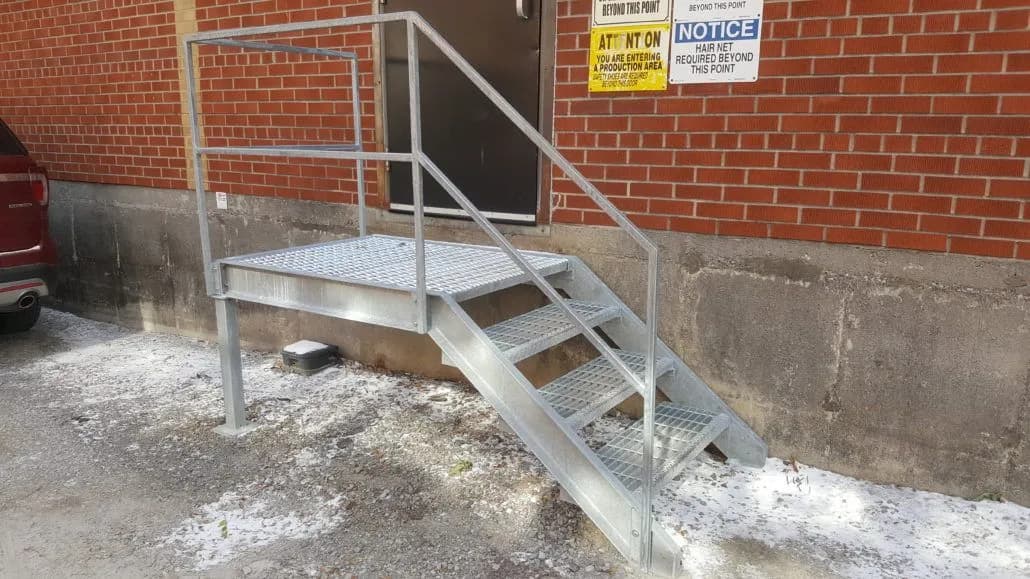 Galvanized steel stair with grating treads and handrails at the rear entrance of a brick building