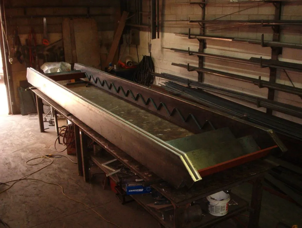 Long steel stair stringer with cut treads resting on trestles in the fabrication shop