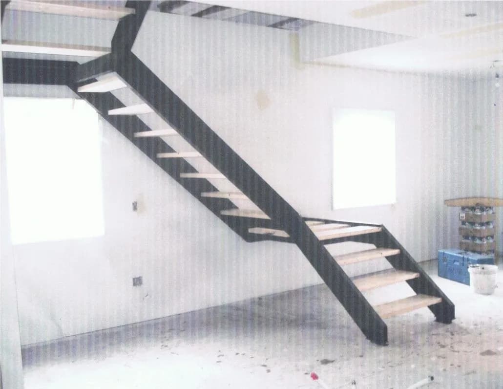 Dark steel staircase with open treads rising through an empty room