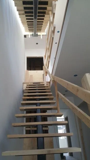 Steel stair stringers carrying wood treads in a narrow open stairwell during construction