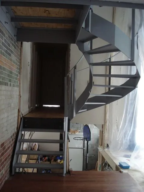 Grey steel spiral staircase with plate treads in a room still under construction